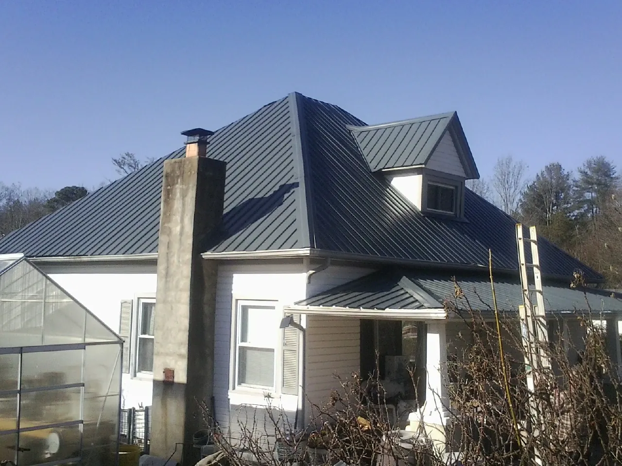 Dark blue standing seam metal roof on a white farmhouse with dormer — Slate & Tile Roof Repair by Roofing Brothers in Popejoy