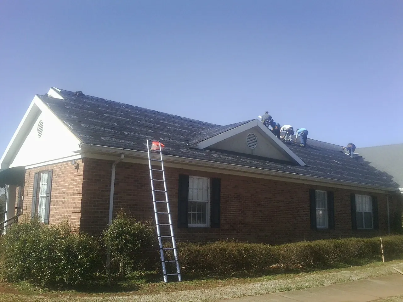 Crew tearing shingles off a brick ranch roof with a ladder set — Emergency Roof Repair work by our crew in Popejoy