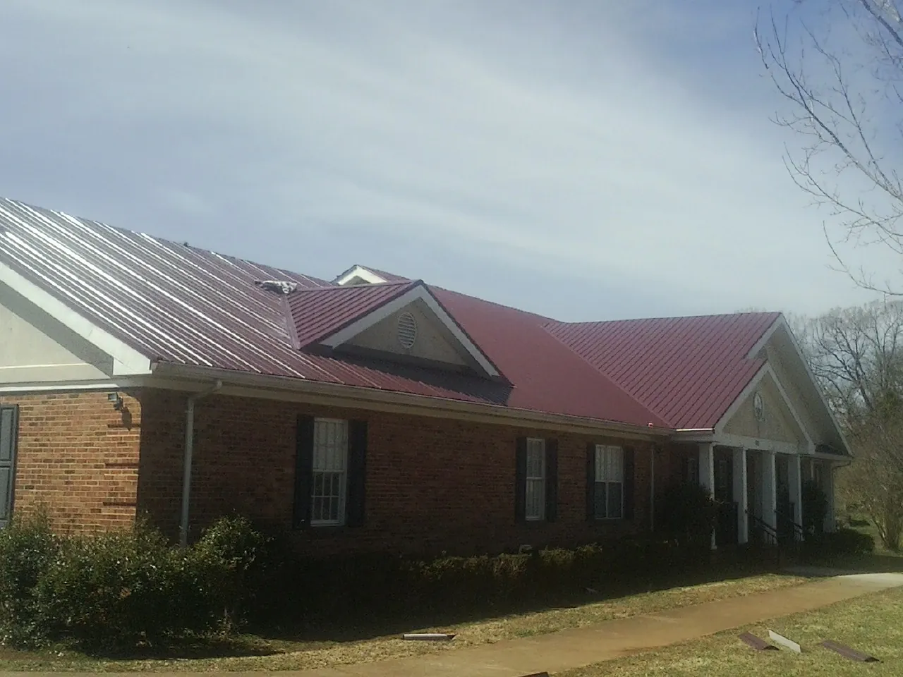 Red metal roof with gabled entries on a long brick building, from a Hail Damage Roof Repair job in Popejoy
