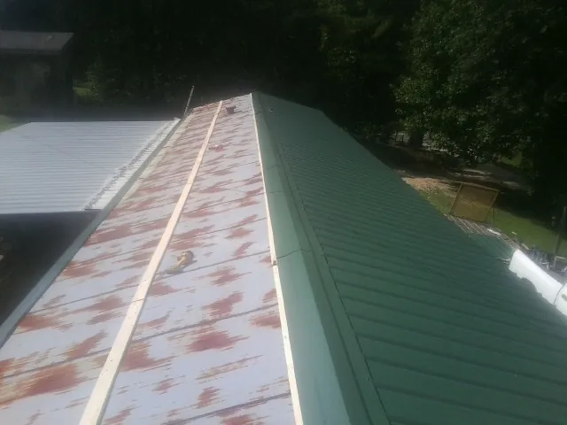 Old rusted panels beside newly installed green metal roofing — Wind Damage Roof Repair by Roofing Brothers in Popejoy
