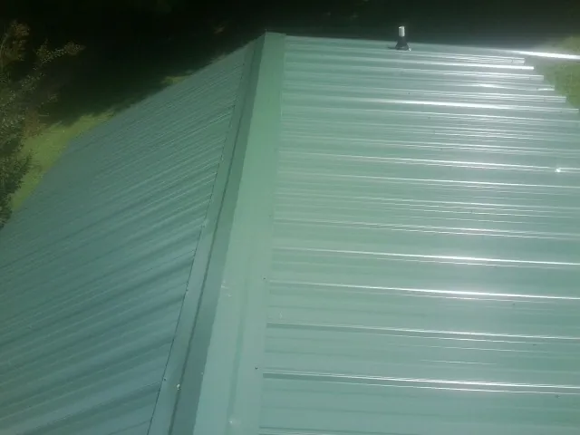 New green metal panels meeting at the ridge of a roof — Flat Roof Repair work by our crew in Popejoy