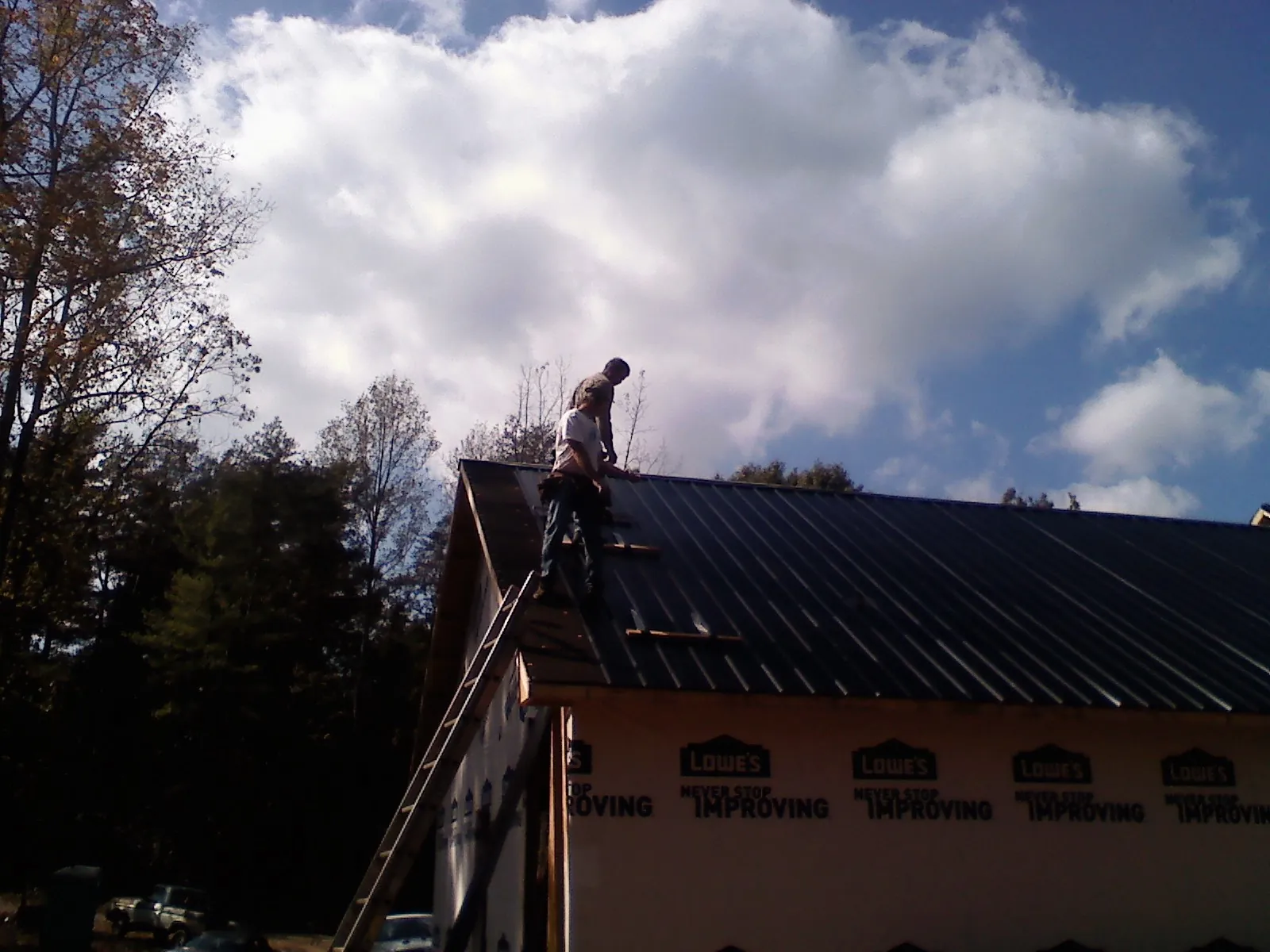 Roofer fastening dark metal panels high against a cloudy sky, from a Roof Inspection job in Popejoy