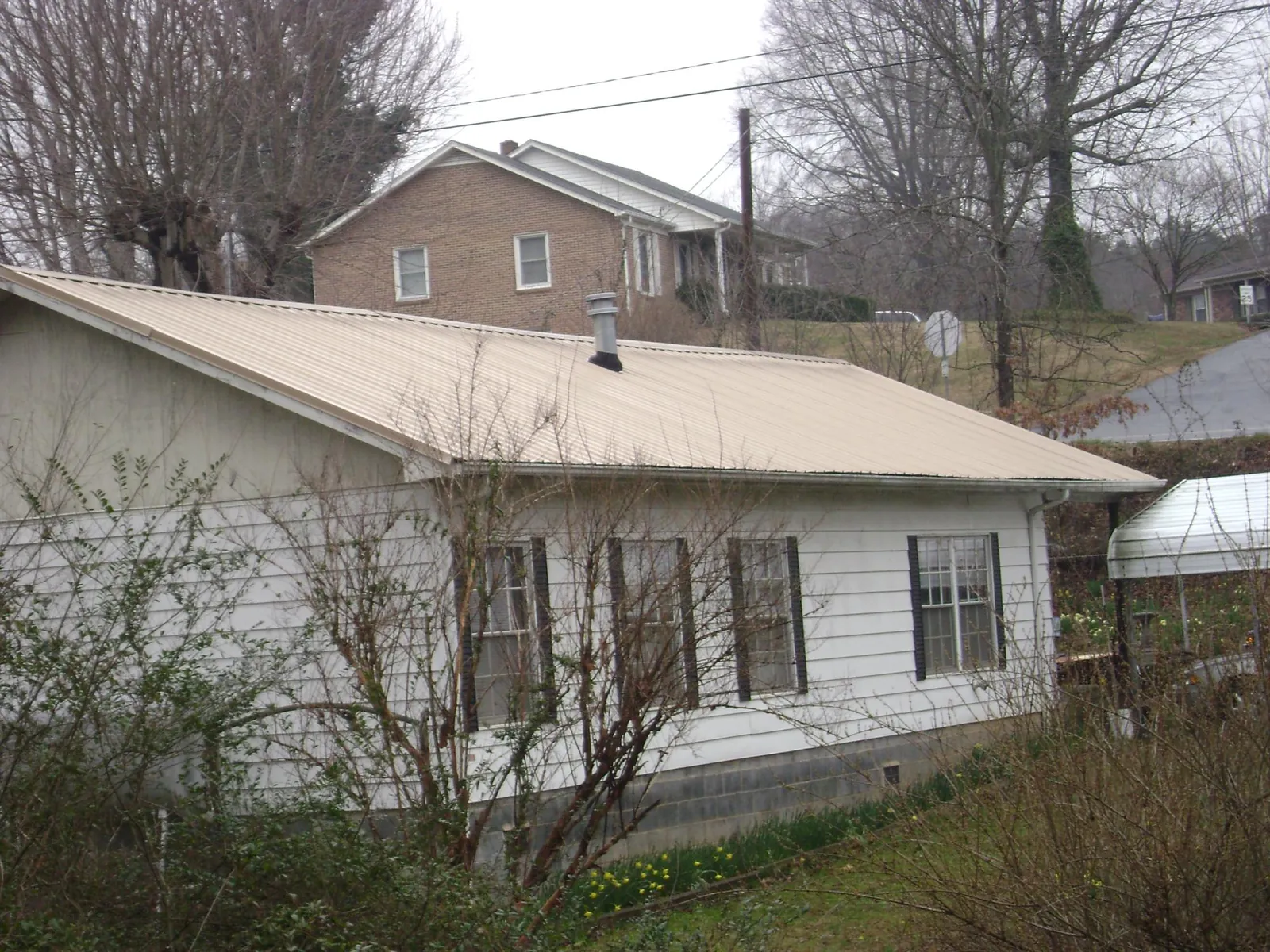Tan metal roof on a white sided house set into a hillside — Commercial Roofing by Roofing Brothers in Popejoy